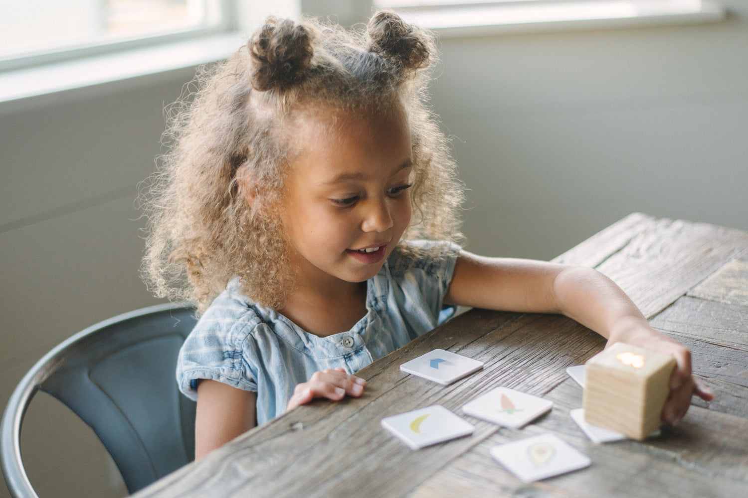 Young girl in a blue shirt playing with Kiri Smart Blocks and Food Tile Pack at a wood table