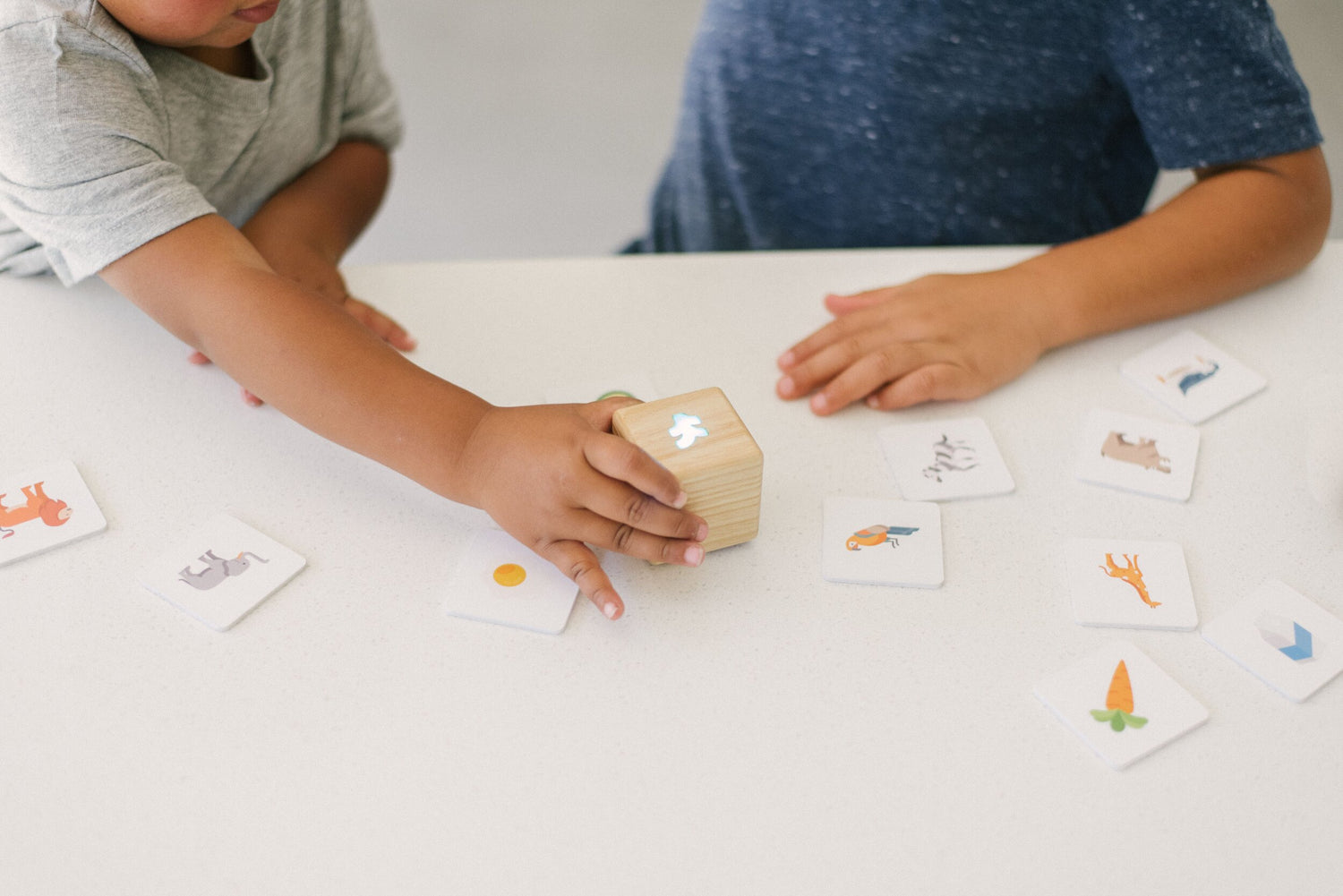 Two young children in t-shirts at a white table playing with Kiri Smart Block and Food Pack tiles